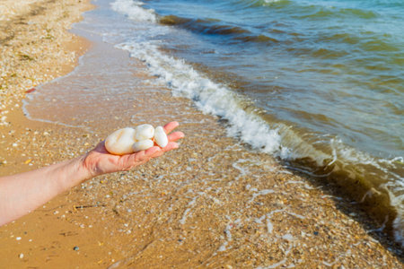 Beautiful view of white stones on female hand on sea waves background. Greece.