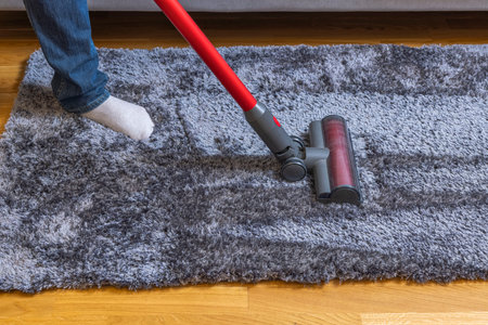 Close up view of man vacuuming of carpet on parquet floor moment. Sweden.