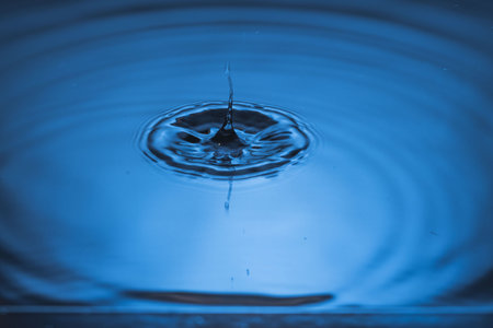 Close up view of drops making circles on blue water surface isolated on background.の写真素材