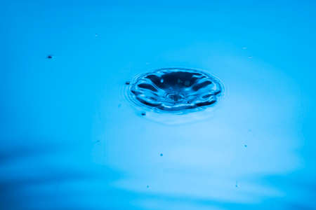 Close up view of drops making circles on blue water surface isolated on blue background.の写真素材