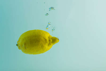 Close up view of lemon falling into water on turquoise background. Gorgeous backgrounds.の写真素材