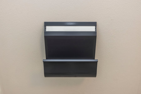 Close up view of dark gray metal newspaper holde on white wall background isolated. Sweden.