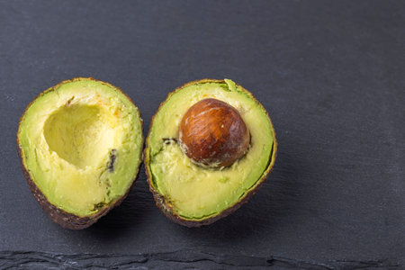 Close up view of cut avocado fruit on black cutting board. Healthy food concept.