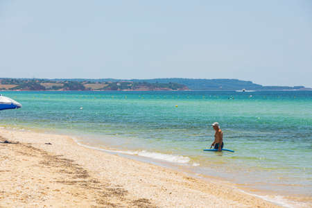 View of old man in blue sea water. Sandy coastline and mountains on background merging to cloudless blue sky. Greece. Nea Potidaea. 08.25.2021.のeditorial素材