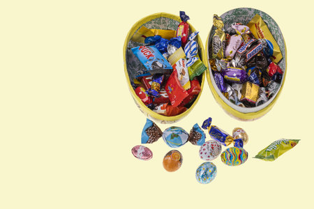 Close up view of an open gift Easter egg with candies inside isolated on yellow background. Sweden....