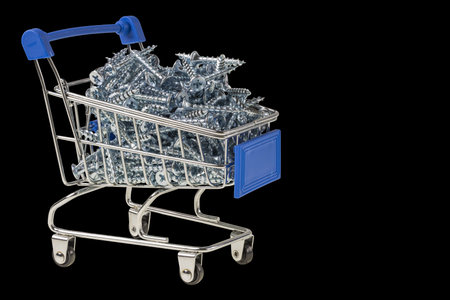 Close up view of toy shopping trolley filled with screws , isolated, on black background.