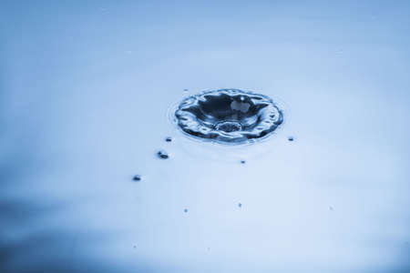 Close up view of falling drops on blue water surface isolated on background.の写真素材