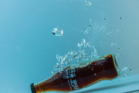 Close up view of bottle of Coca cola falling into water isolated on blue background. Sweden....