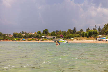 Beautiful view of people swimming in sea and sandy beach with green plants on background. Greece. Nea Potidea. 07.10.2021.のeditorial素材