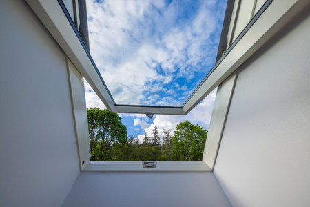 Beautiful view from dormer roof window in house to tops of forest trees against background of blue sky with white clouds. Sweden.の写真素材