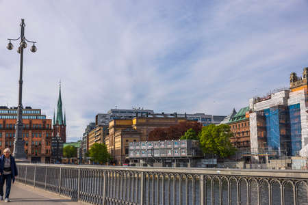 Beautiful Stockholm cityscape. old woman walking on bridge. Vintage church between beautiful buildings on cloudy sky background. Sweden. Stockholm. 05.18.2022.のeditorial素材