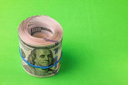 Close up view of stack of 100 dollar bills rolled into roll isolated on green background. Sweden.