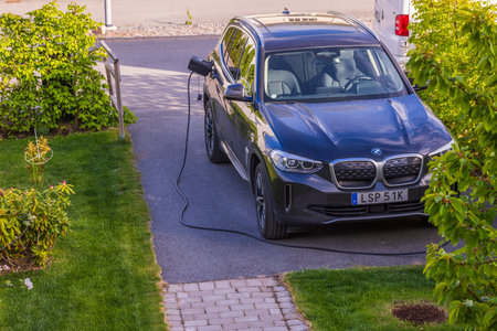 Close up view of BMW ix3 electric car with charging cable in a private parking lot. Sweden. uppsala. 06.12.2022.のeditorial素材