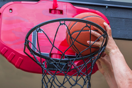 Close up view of man throwing ball into basketball hoop with net while playing basketball. Sweden.