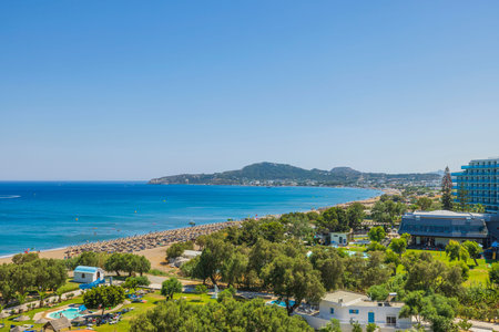 Beautiful view of Mediterranean sea sand beach with sun beds and sun umbrellas and hotel buildings on background. Rhodes. Greece. 07.25.2022.のeditorial素材