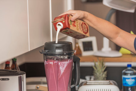 Close up view of female's hand pouring milk into blender with smoothie. Sweden. uppsala. 07.25.2022.のeditorial素材