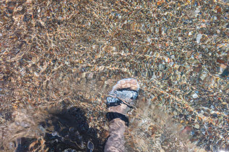 Close up view of foot in sandals through rolling waves. Summer tourism concept. Greece.の写真素材