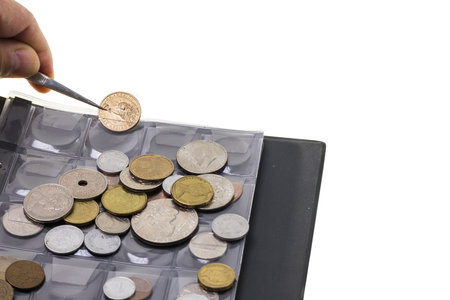 Close up view of tweezers in man's hand holding coin over coin collection. Numismatic concept.