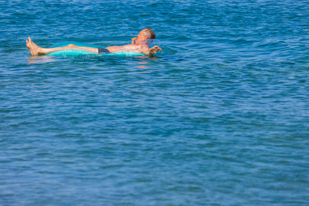 Close up view of man on inflatable mattress on blue water surface. Rhodes. Greece. 07.15.2022の写真素材