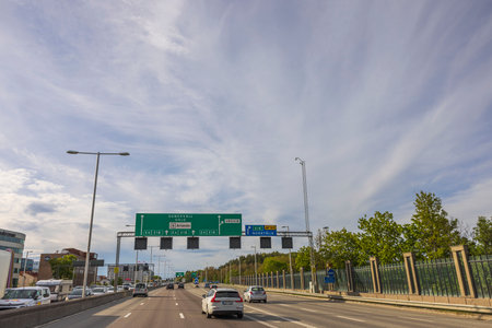 Cityscape view of multi-lane road merging with cloudy blue sky on horizon. Green road signs over road lanes. Sweden. Stockholm. Europe. 05.18.2022.のeditorial素材