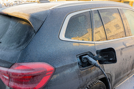 Close up view of electric car connected by cable from charging station on frosty winter day. Sweden.