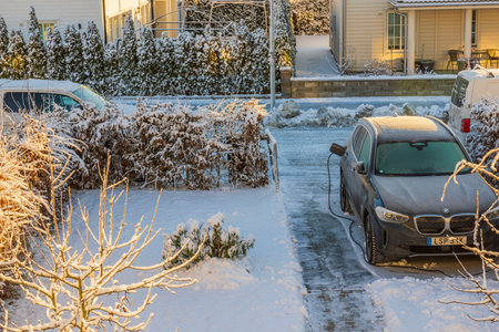 Beautiful view of parking lot in private house with BMW IX4 electric car connected by cable from charging station on frosty winter day. Sweden. uppsala. 12.26.2022.のeditorial素材