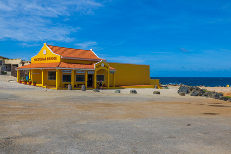 Beautiful view of yellow building of Natural Bridge boutique for tourists on Atlantic Ocean coastline of Aruba. Oranjestad. 02.16.2023.のeditorial素材