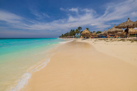 Beautiful view of Atlantic ocean with people lying on sun loungers under sun umbrellas on sandy Eagle beach. Aruba. Oranjestad. 03.18.2023.のeditorial素材