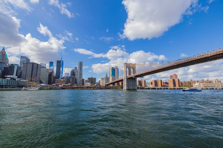 Beautiful panoramic view of Brooklyn Bridge over Hudson River and skyscrapers of Manhattan on against blue sky with white clouds. USA. NY. 09.21.2022.のeditorial素材