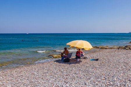 Beautiful view of family and man fishing on coastline of Mediterranean sitting under sun umbrella. Greece.の写真素材