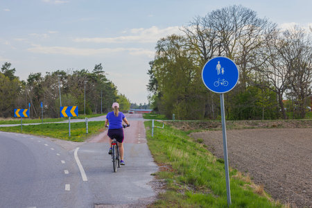 View of woman on bicycle moving along cycle road against backdrop of beautiful countryside. Sweden.の写真素材