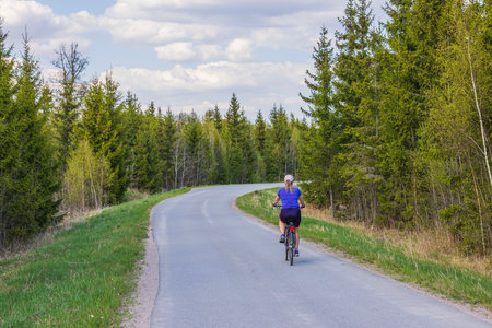 View of woman on bicycle moving along asphalt cycling road against backdrop of forest on both sides. Sweden.の写真素材