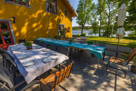 Beautiful view of villa with outdoor party tables covered with table cloth ready served. Green trees on lake background. Sweden. Europe.の写真素材