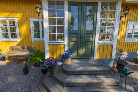 Beautiful view of exterior of entrance with wooden porch to villa decorated with vases of fresh flowers.の写真素材