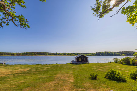 Beautiful view of small utility house on lake shore on blue sky background. Sweden, Europe.の写真素材