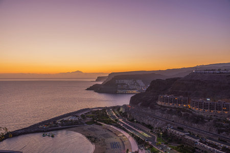 Beautiful view of buildings and sand beach situated on mountain landscape of Gran Canaria Island on backdrop of sunset in Atlantic Ocean.の写真素材