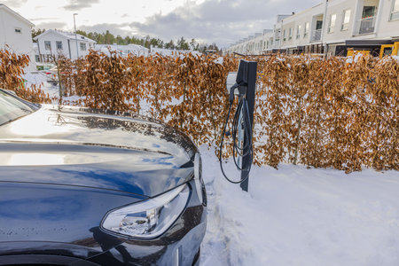Close-up view of electric car in private parking lot at home with charging station on frosty winter day.の写真素材