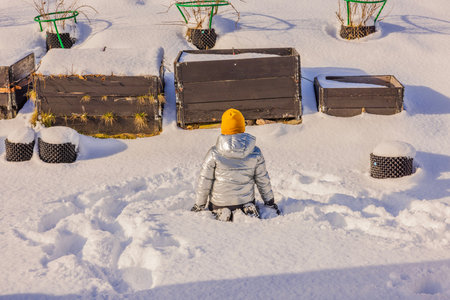 Beautiful view of child sitting in snow on backyard on bright winter day. Sweden.