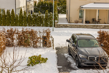 View of parking lot with electric car connected by cable from charging station winter day. Sweden.の写真素材