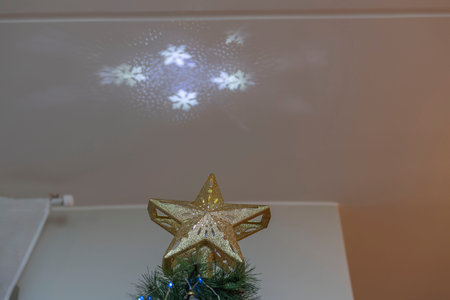 Beautiful view of gold star electrical top on Christmas tree that projects snow flakes on ceiling.