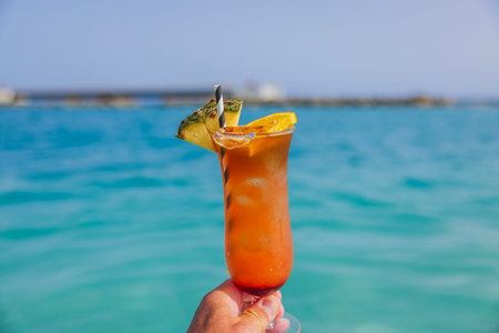 Close-up view of man's hand holding a glass of alcoholic cocktail on  background of blue water of Caribbean Sea.の写真素材