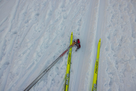 Close-up view of yellow classic plastic Fischer skis and Swix poles lying on ski track.のeditorial素材