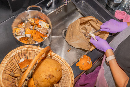 Close up view of female hands in rubber gloves cleaning mushrooms in kitchen sinkの写真素材