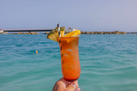 View of man's hand holding a glass of alcoholic cocktail on  background of blue water of Caribbean Sea.の写真素材