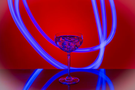 Beautiful view of alcohol drink with ice cubes in crystal glass on red background.の写真素材