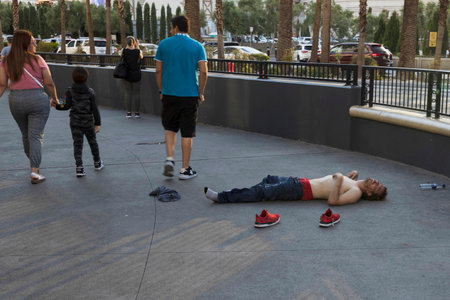 View of an alcoholic man sleeping on Las Vegas Strip as family with young child passes by. Impact of addiction concept. Las Vegas. USA.のeditorial素材