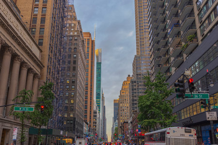View of 36th Street in Manhattan with skyscrapers and bustling with transportation, set against backdrop of blue sky with white clouds. New York. USAのeditorial素材