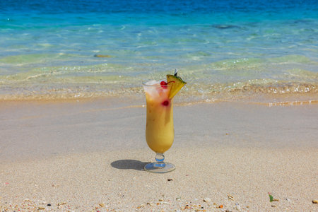 Close up view of glass with alcoholic cocktail stands on sandy beach of Caribbean Sea on island of Curacao.の写真素材