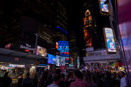 People stroll through night on Broadway in Manhattan, surrounded by glow of LED panels and towering...