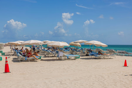 Stunning vista of white sandy beach along Atlantic Ocean with people relaxing on sun loungers beneath umbrellas. Miami Beach. USA.のeditorial素材